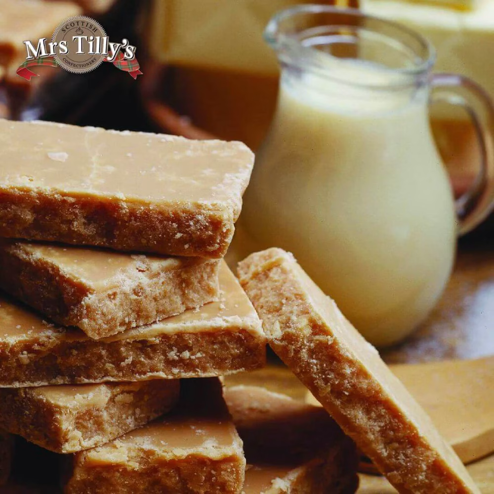 A stack of traditional Scottish tablet by Mrs Tilly's, featuring rich, crumbly, golden fudge-like pieces with a creamy texture. A jug of milk sits in the background, enhancing the warm, homemade feel.